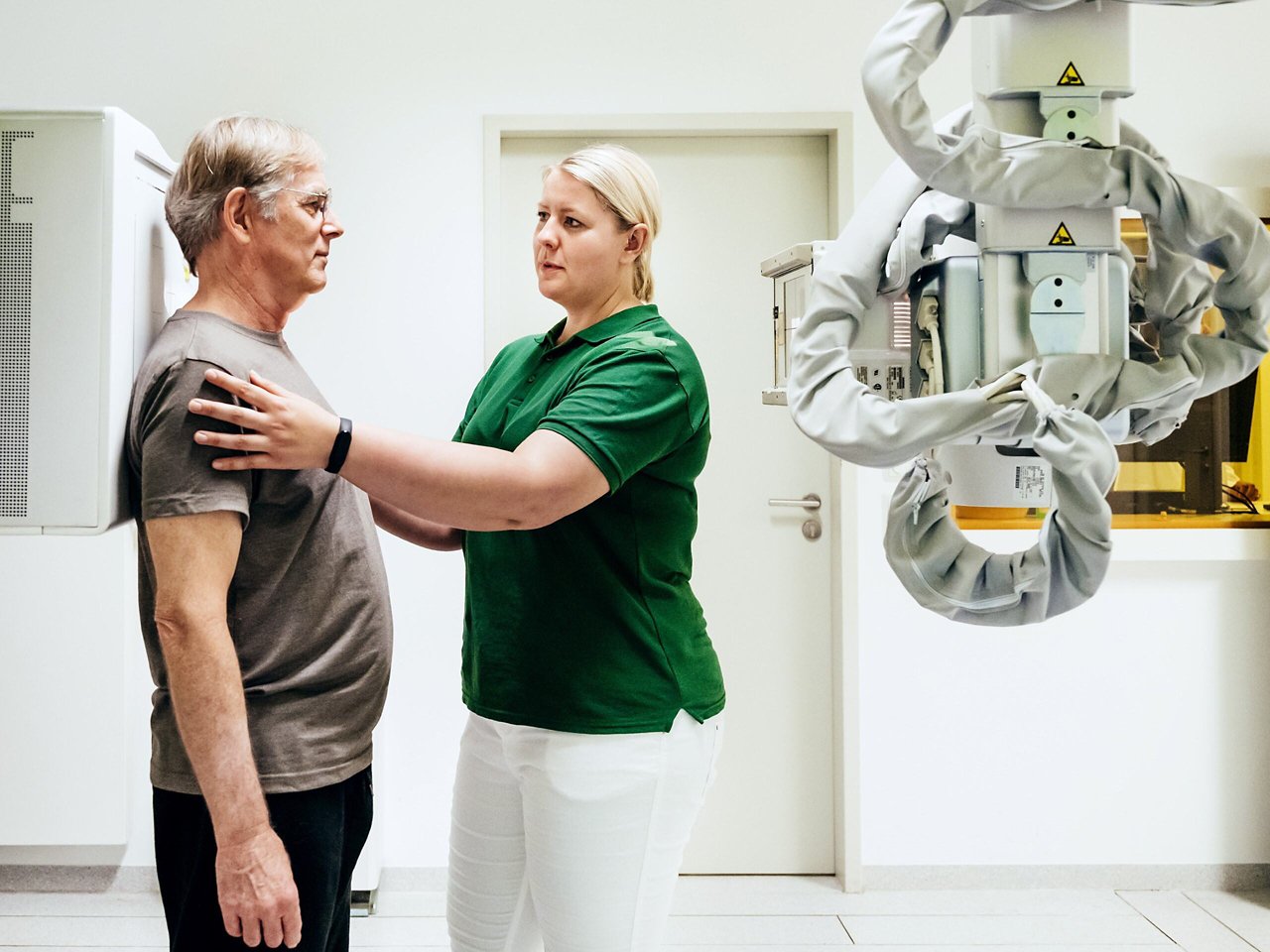 An imaging technician touching a patient's shoulders to position him for an x-ray