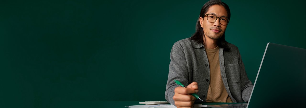 Portrait of a male hospital buyer at his desk on a dark green background.